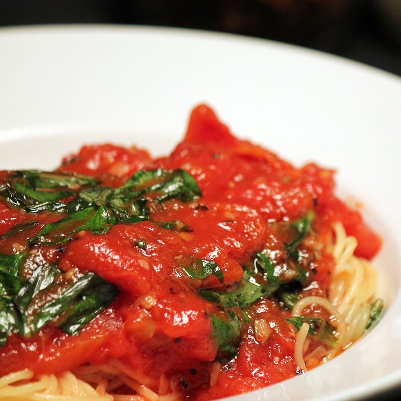 Close-up of Romano's spaghetti with rich red tomato sauce and fresh green basil in a white bowl.
