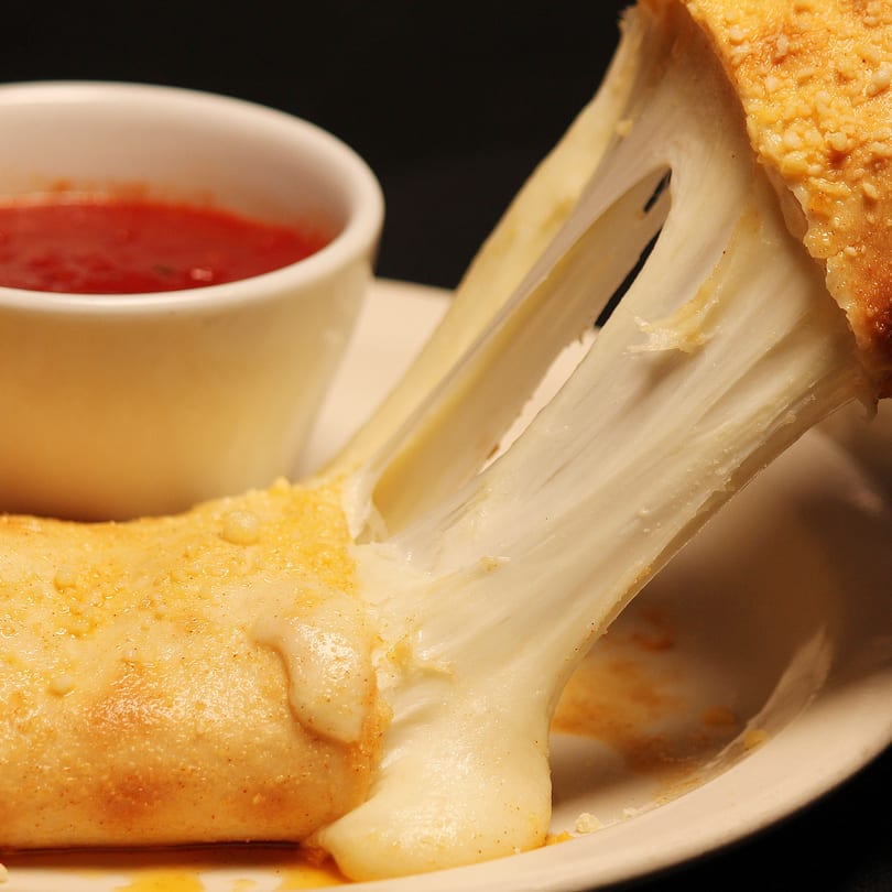 Stretchy melted mozzarella cheese pulling from a Romano's Chicago Pizzeria breadstick, with marinara sauce.