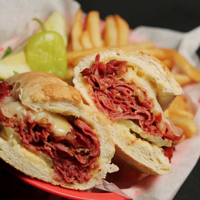 A Romano's Chicago Pizzeria Italian beef sandwich, cut in half, with fries and pickles.