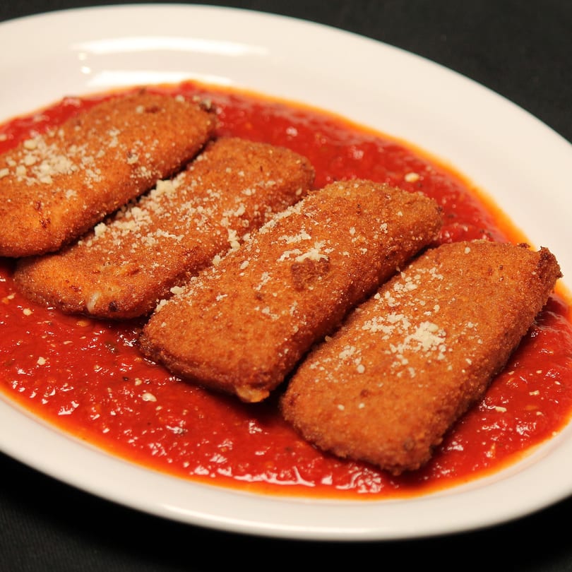 Four golden-brown fried ravioli, sprinkled with Parmesan, resting in a vibrant red marinara sauce on a white plate.