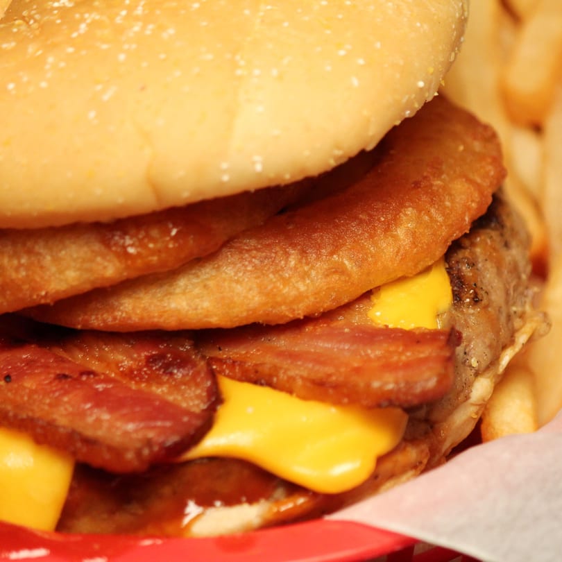 Close-up of a Romano's burger with bacon, melted cheese, and onion rings on a bun.