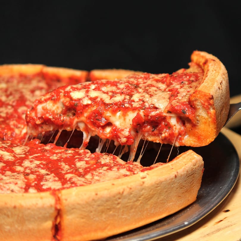 A slice of Romano's Chicago Pizzeria deep-dish pizza being lifted, with cheese stretching.